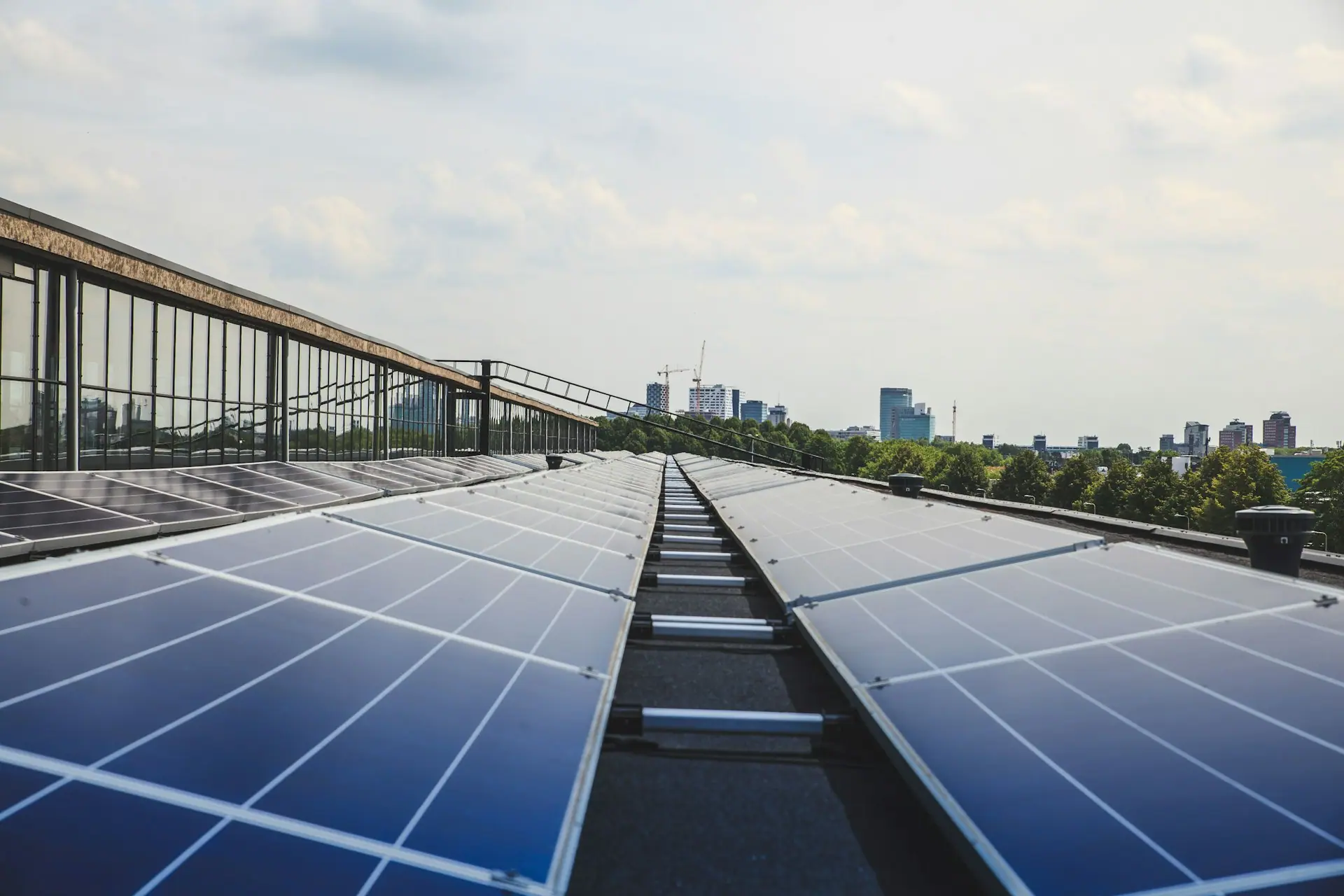 Rows of photovoltaic panels on a commercial rooftop running towards a city skyline in afternoon light