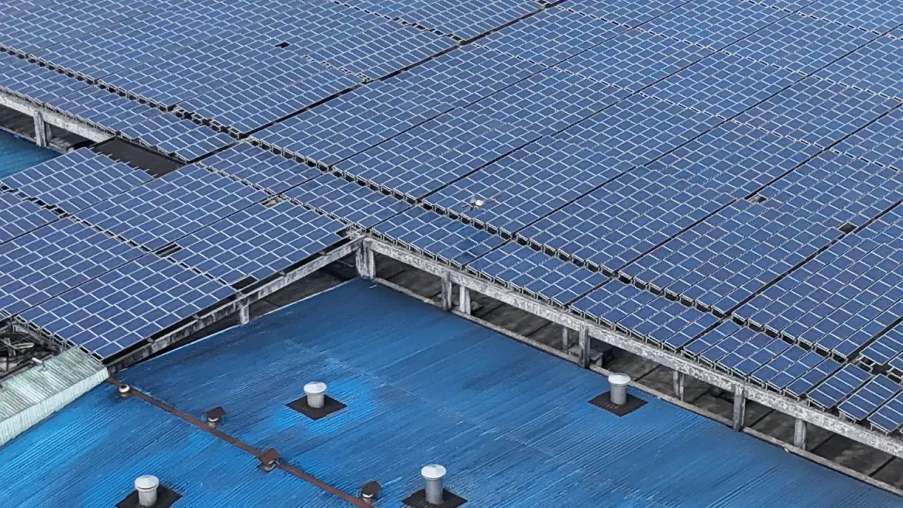 Close aerial view of panel rows laid across a blue profiled-sheet industrial roof