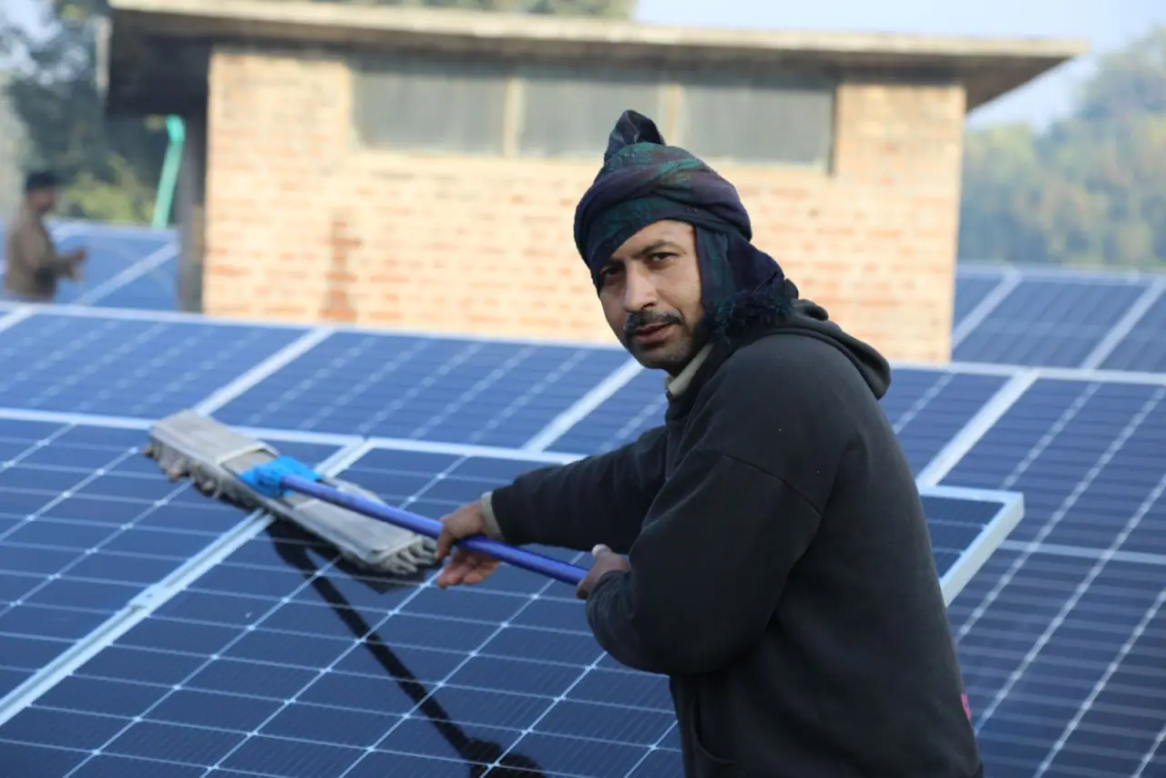 A technician cleaning the surface of a rooftop solar array with a water-fed brush